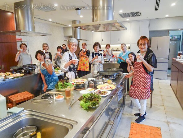 調理台を囲んでコンベ（乾杯）！！！　みなさんの笑顔はチェゴ（最高）♪　「チャㇽ　モッケッスㇺニダ」